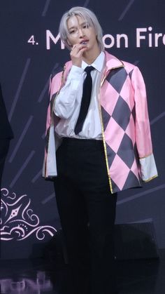 a man in a pink jacket and tie standing on stage with his hand to his mouth