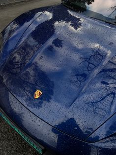 a blue sports car parked on the side of the road with trees reflected in it