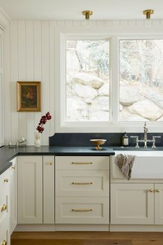 a white kitchen with black counter tops and gold pulls on the cabinet doors is pictured in this image