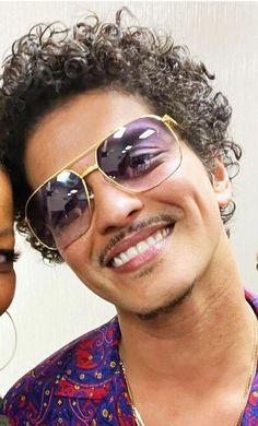 a man and woman are smiling for the camera with sunglasses on their faces, one is wearing a purple shirt