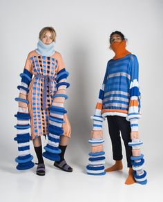 two women in colorful clothing standing next to each other on a white background with one woman wearing an orange and blue striped sweater