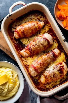 two sausages in a casserole dish with carrots and mashed potatoes