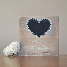 a wooden sign with a black heart on it next to a white rose and the words, weeks until our baby is due