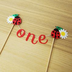 two ladybug cake toppers with the word one spelled out in red and daisies