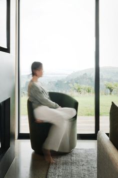 a woman sitting in a chair looking out the window with her foot on the couch