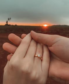 two people holding each other's hands in front of an orange sky at sunset