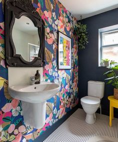 a colorful bathroom with floral wallpaper and white toilet, sink and mirror on the wall