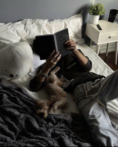 a person laying on a bed reading a book with a dog sitting next to them