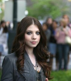 a woman with long brown hair and blue eyes is standing in front of a crowd