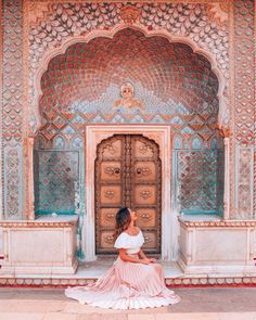 a woman sitting on the ground in front of an ornate building with doors and windows