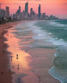 people walking on the beach in front of some tall buildings at sunset or sunrise time