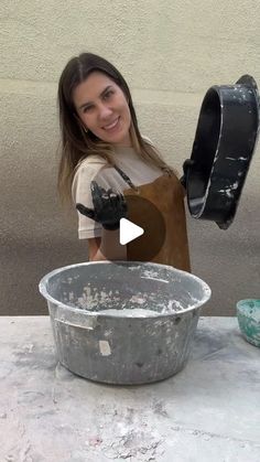 a woman in an apron is holding a bucket and smiling at the camera while standing next to a large metal bowl