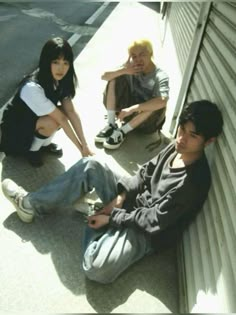 three young people sitting on the side of a building