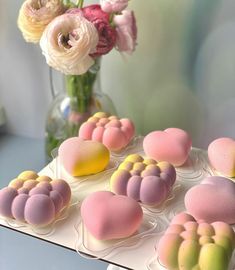 some pink and yellow heart shaped cookies are on a tray next to a vase with flowers