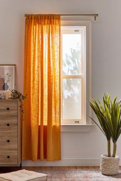 an orange curtain hanging in front of a window with a potted plant next to it