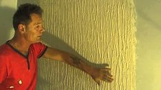 a man in a red shirt leaning against a wall with his hand on the wall