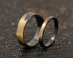 two gold wedding rings sitting on top of a black table next to each other,