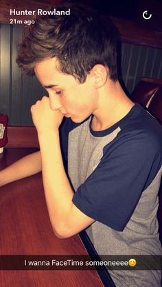 a young man sitting at a wooden table with his hand on his face and looking down