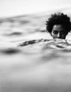 a woman swimming in the ocean with an afro hairdow on her head and looking at the camera