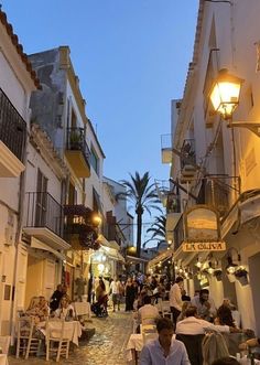 people sitting at tables in an alleyway with palm trees on either side and buildings lining the street