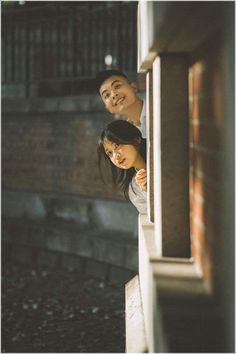 two people standing next to each other looking out the window