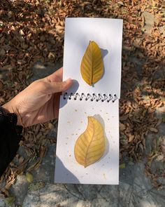 a person holding up a piece of paper with two yellow leaves on top of it