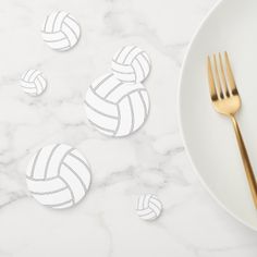 white plates with gold forks and silverware on a marble counter top next to volleyball shaped coasters