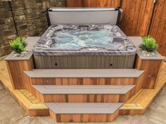 a hot tub sitting on top of a wooden platform next to a brick wall and green plants