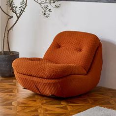 an orange chair sitting on top of a wooden floor next to a potted plant