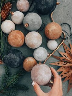 a person holding some ornaments in their hand next to pine cones and other decorations on the ground