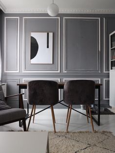 two chairs sitting in front of a table with a painting on the wall behind them