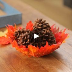 two pine cones sitting on top of a wooden table next to an orange and red leaf