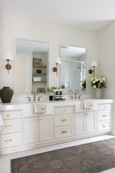 a white bathroom with two sinks and large mirrors on the wall, along with an area rug in front of it