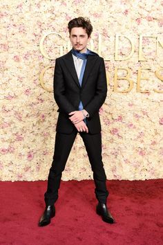 a man in a suit and tie standing on a red carpet with his hands behind his back