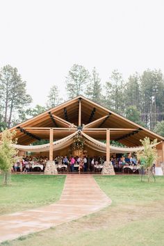 a group of people sitting at tables under a wooden structure in the middle of a field