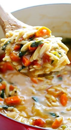 a ladle full of pasta and vegetables being held by a wooden spoon over a red pot