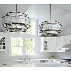 two chandeliers hanging from the ceiling in a white kitchen with marble counter tops