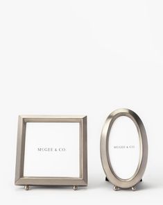 two silver frames sitting next to each other on top of a white surface with the word mcgoie & co written in it