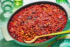 a pot filled with beans and vegetables next to glasses of water on a table top