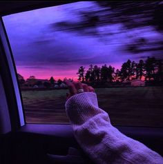 a person's hand in the passenger seat of a car at dusk with purple clouds