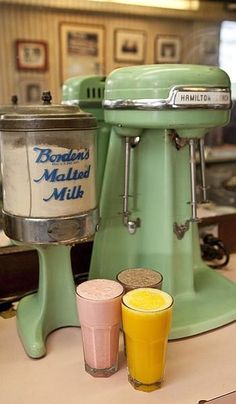 a green mixer sitting on top of a counter next to two glasses filled with orange juice