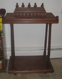 a wooden table with an ornate top and shelf on the floor next to a wall