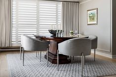 a dining room table with four chairs and a rug in front of the window that has vertical blinds