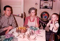 an older woman blowing out candles on a birthday cake with two young boys sitting at the table