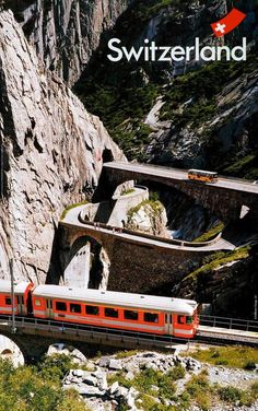 a red and white train traveling down tracks next to a mountain covered in rocks with a bridge