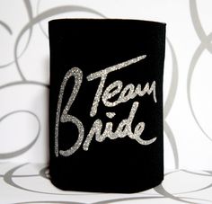 a black can cooler with the word team bride written in silver glitter on it's side