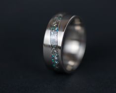 a wedding band with blue and green glitter inlaying the center, on a black background