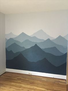 an empty room with mountains painted on the wall and wood flooring in front of it