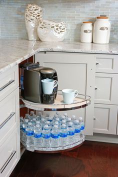 a shelf with water bottles and cups on it in a kitchen next to white cabinets