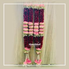 two rows of pink and white flowers are arranged on the side of a wall in front of a curtain